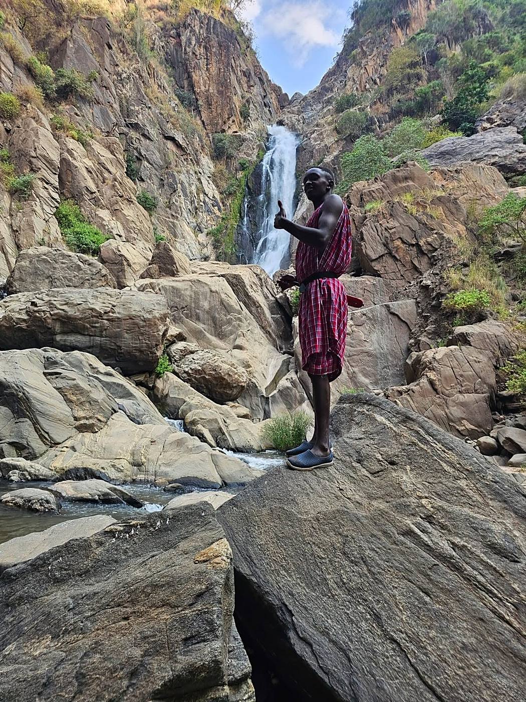 Maasai guide in traditional shuka standing on rocks before a waterfall